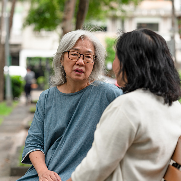 Two close senior friends are sitting on a park bench, spending time together talking about legal advice.