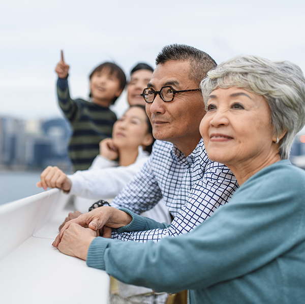 Relaxed senior Chinese woman and husband enjoying Hong Kong views with extended family at Ocean Terminal Deck atop Harbour City Shopping Centre.