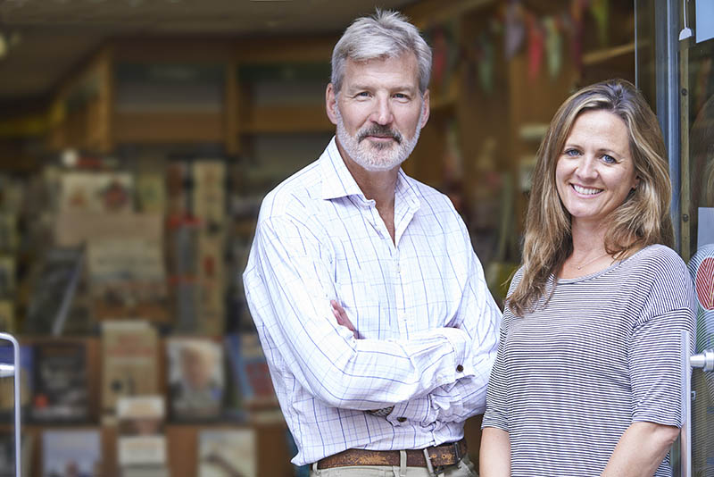 Husband and wife business owners smiling in front of their store