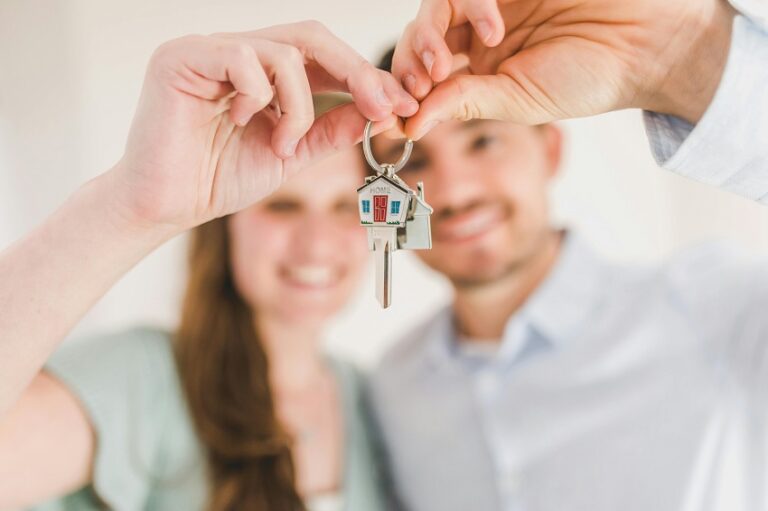 A man and a woman hold a key chain with a little house and one key. Each person has their thumb and finger on the key.